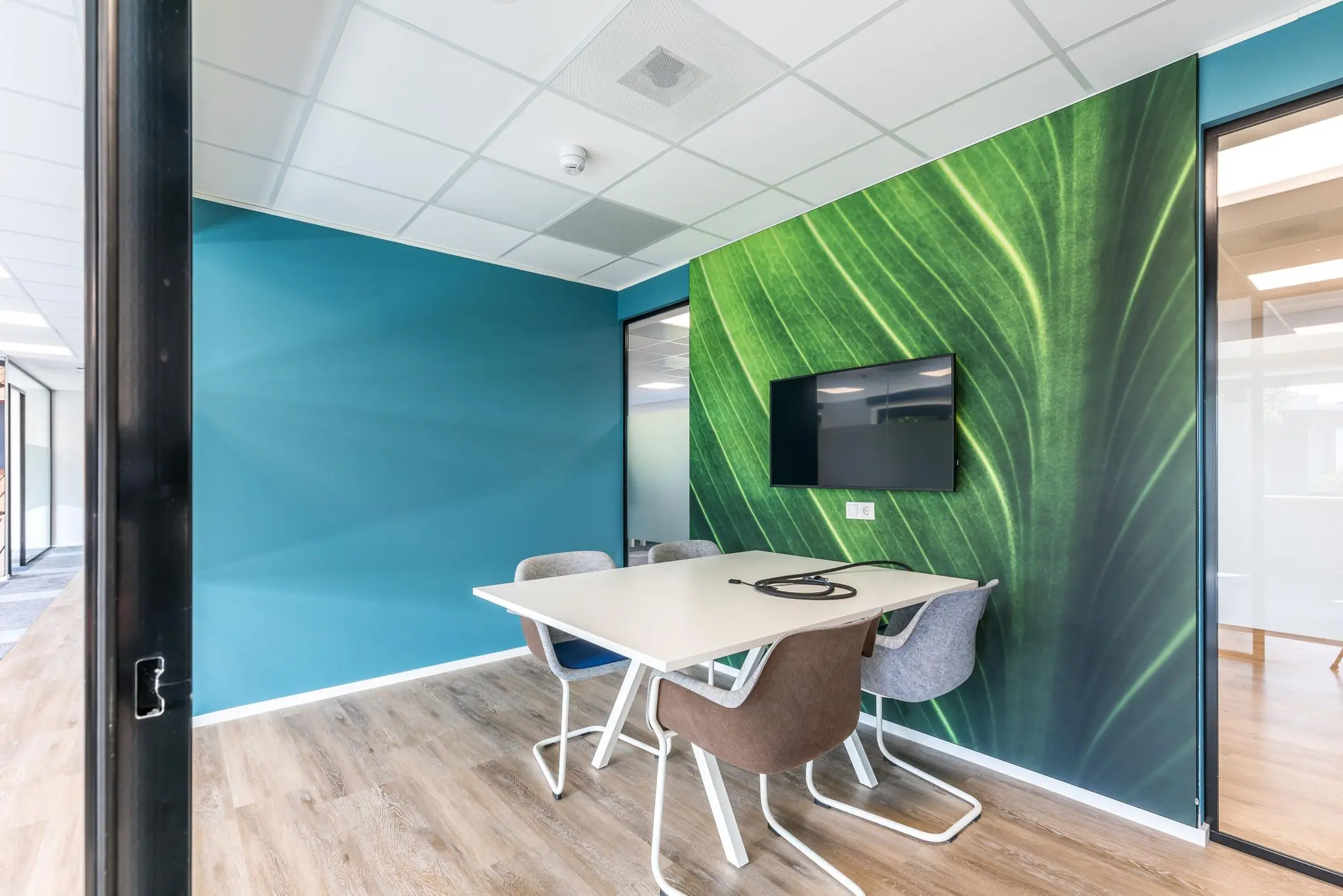 Moderne vergaderruimte aan de Baarnsche Dijk met een groene bladprint op de muur, een scherm en vier stoelen rond een witte tafel.